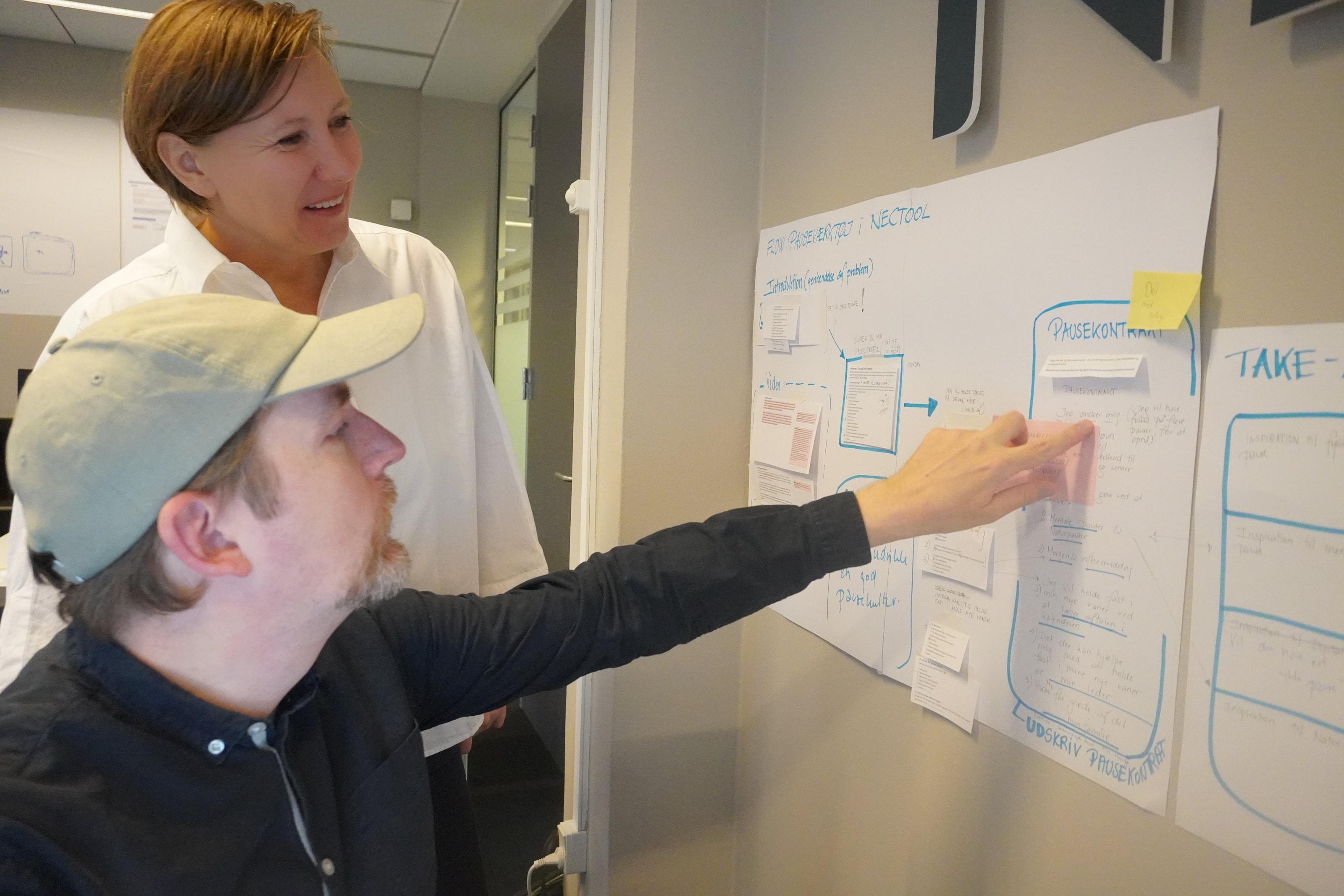 Two people going through a customer journey map pinned to the wall